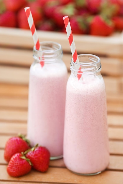 Two milkshakes from fresh strawberries in mini glass bottles with striped tubes