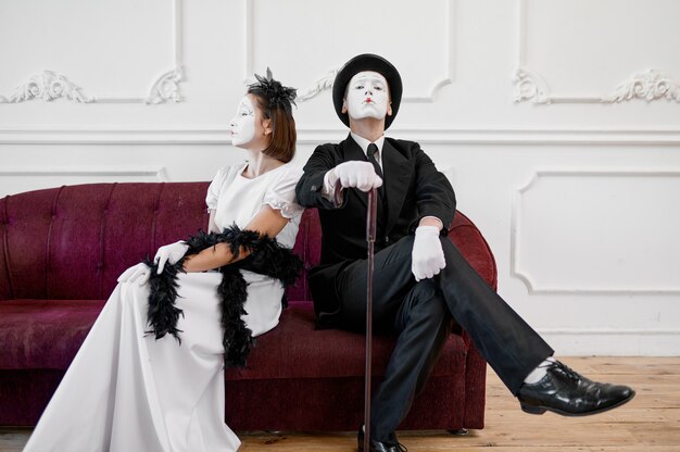 Two mime artists, lady and gentleman sitting on sofa