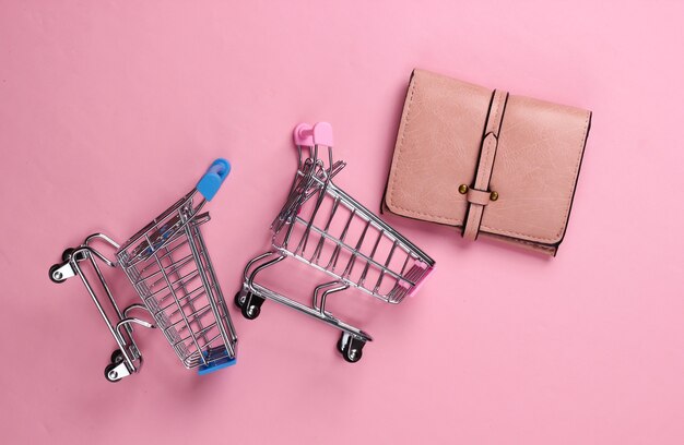 Two mini supermarket trolleys with wallet on pink pastel