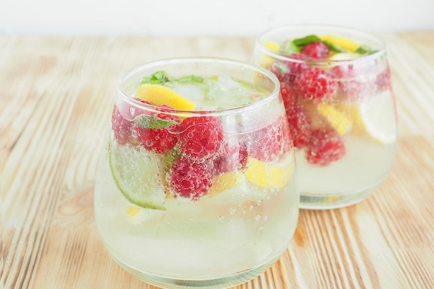 Two misted glasses with ice lemonade and fruits and berries lemon, lime and mint in soda bubbles. summer cooling drink.
