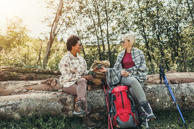 Two mixed-race female friends takes a tea break partway through their hike in the forest.