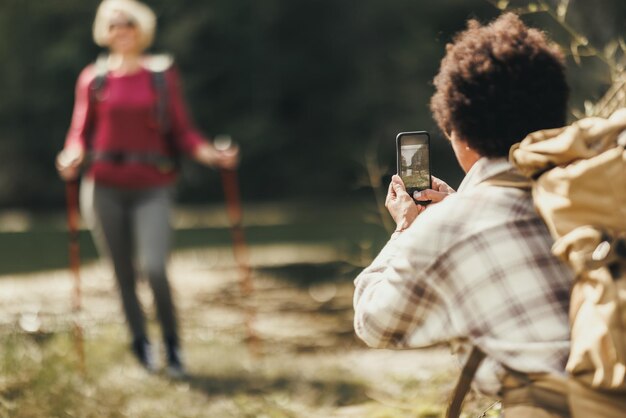 Two mixed-race female friends taking a photos of each other with a smartphone during a hike.