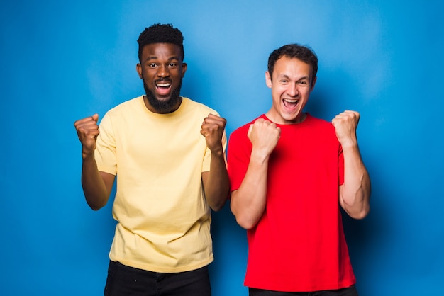Photo two mixed race men with win gesture isolated on blue wall