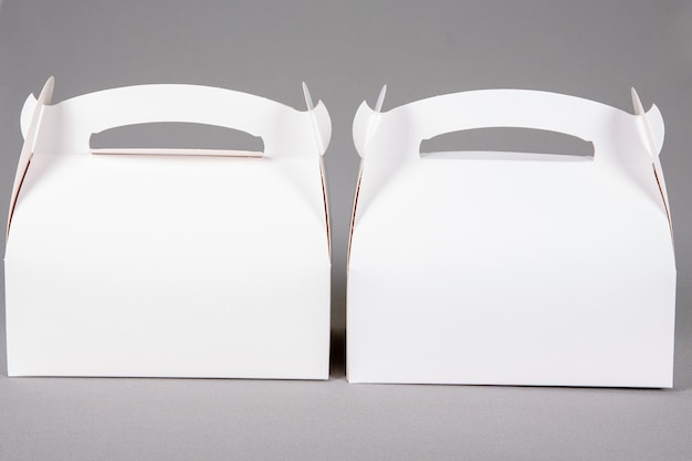 Два макета белой пустой бумажной упаковки для пекарни, большая и маленькая коробка с ручкой на сером фоне