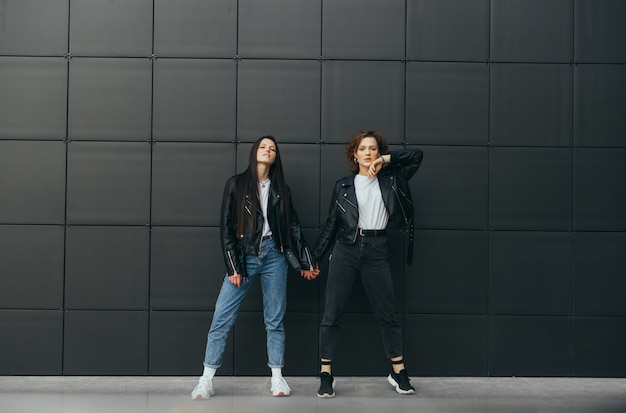 Two models in street clothes posing against a dark wall