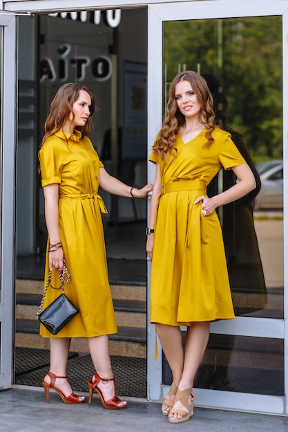 Two models on the street in mustard colored dresses