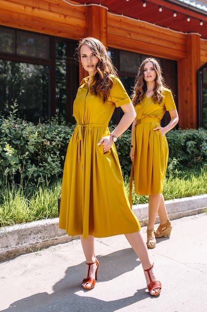 Two models on the street in mustard colored dresses