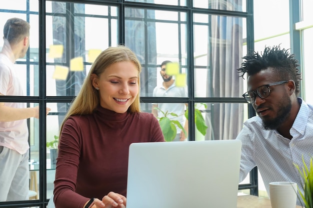 Two modern business people discussing documents and other working moments in office with collegues on the background