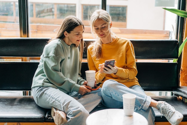 two modern confident women friends in a coffee shop communicate and chat on the phone