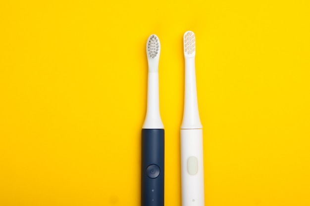 Two Modern electric toothbrushes on yellow surface