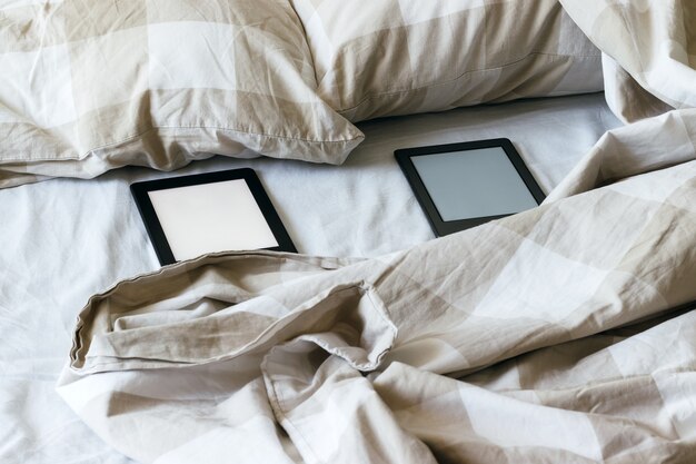 Due libri elettronici moderni con schermi vuoti vuoti su un letto bianco e beige.