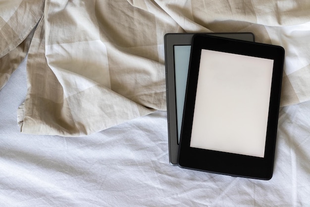 Two modern electronic books with blank screens on white and beige bed mockup tablets