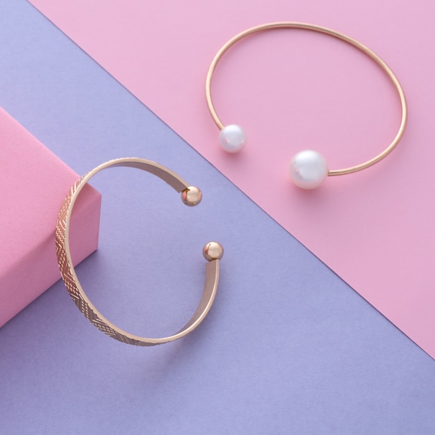 Two modern gold with pearl and classic bracelets on diagonal pastel colors background