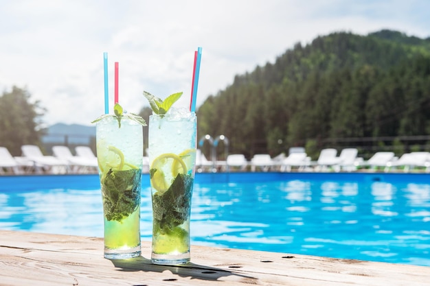 Two mojito cocktail with lime and mint in highball glass at the swiming pool background on summer mo