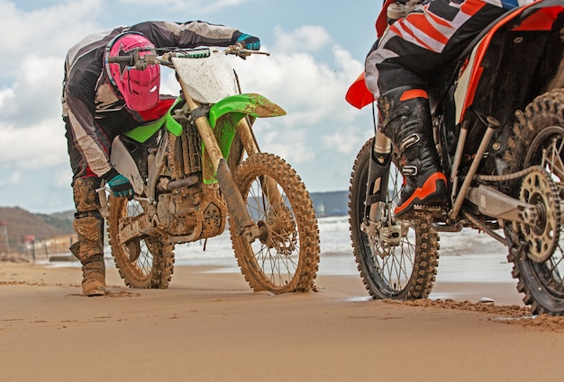 Two Motorcyclists in a protective suit sitting on motorbikes opposite each other in front of the sea