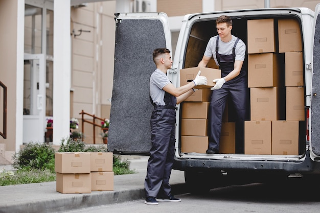 Two movers wearing uniforms are unloading the van full of boxes House move mover service