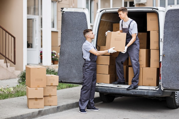 Two movers wearing uniforms are unloading the van full of boxes House move mover service