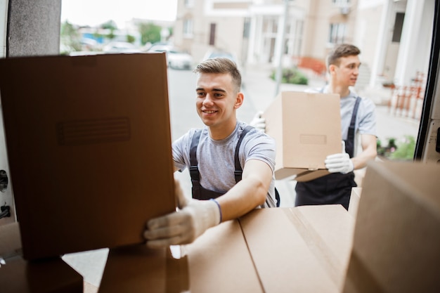 Two  movers wearing uniforms are unloading the van full of boxes