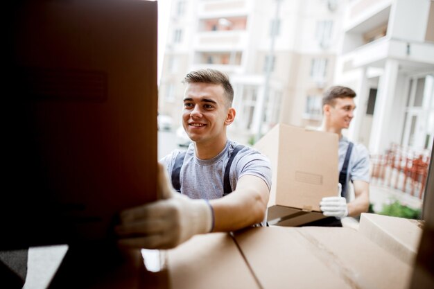 Two  movers wearing uniforms are unloading the van full of boxes