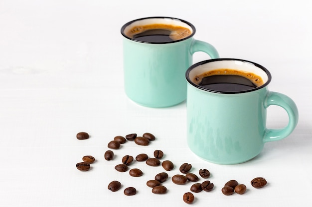 Two mugs of fresh aromatic coffee with grains on white wooden table