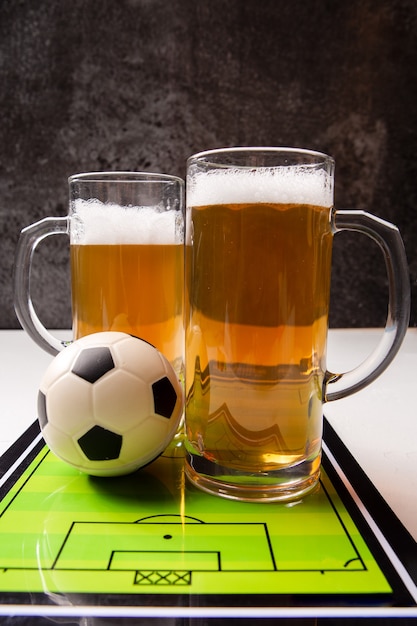 Two mugs of frothy beer, table football, ball on white table