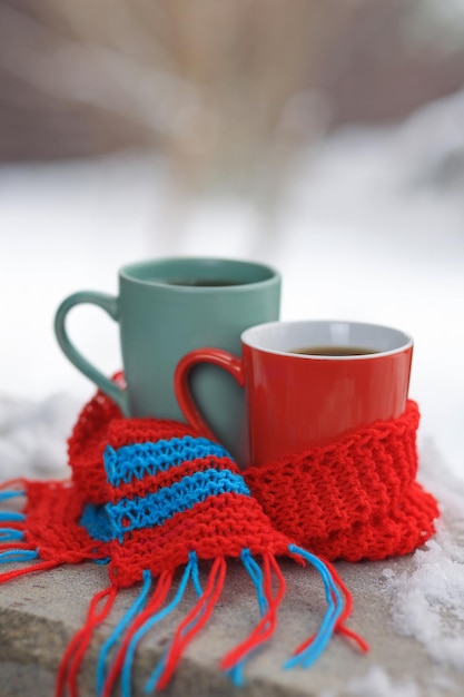 Two mugs of hot tea wrapped in a knitted scarf outside in winter Selective focus