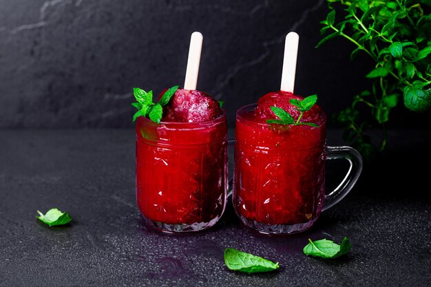 Two mugs of refreshing raspberry smoothie with ice cream and mint on the dark table. Unusual serving of summer cocktails.