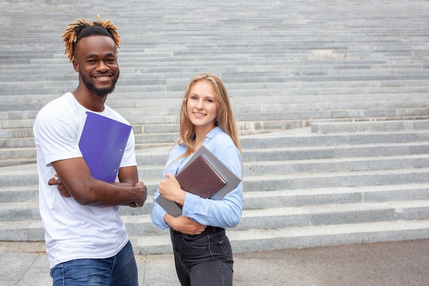 Two multiethnic friends students with lucky faces posing outdoors