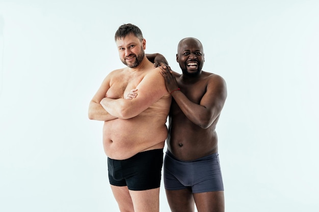 Two multiethnic men posing for a male edition body positive beauty set. Shirtless guys with different age, and body wearing boxers underwear