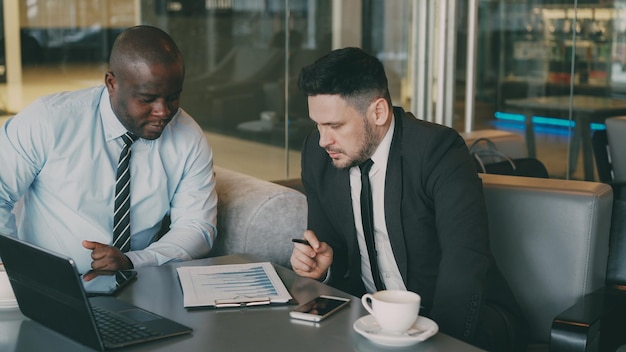 Two multiethnic partners in formal clothes sitting and discussing financial charts details