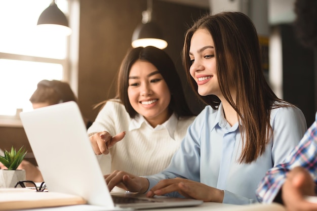 two multiethnic women are seated at a desk in a welllit library working together on a project one is
