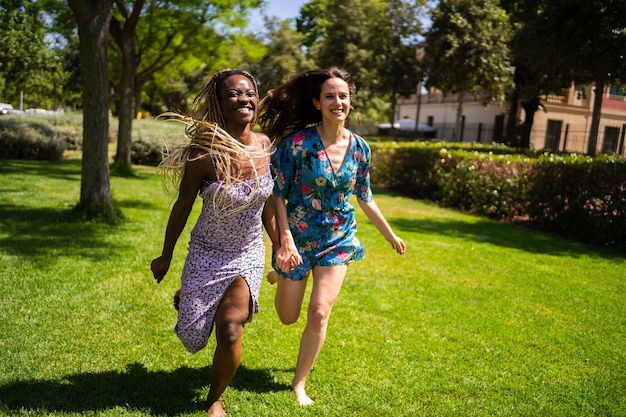 Two multiethnic women running holding hands outdoors