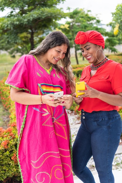 Two multiethnic women standing in park looking at cell phone and talking