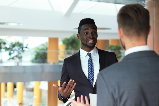 Two multinational young businessmen discussing business at meeting in office.