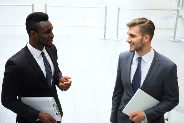 two multinational young businessmen talking while stairs in modern office building.
