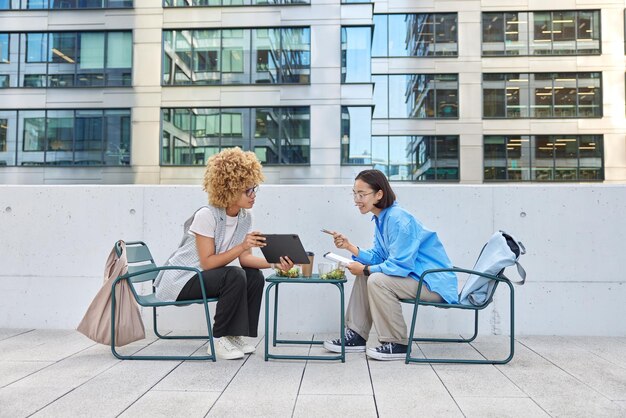 Two multiracial students in smart casual clothes enjoy\
corporate friendship prepare project surf internet via digital\
tablet have interesting discussion discuss something cooperation\
and team work