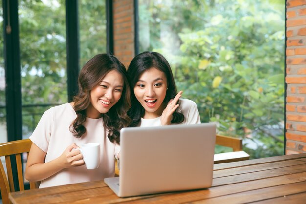 Due giovani amiche multirazziali che navigano in internet insieme su un laptop mentre si siedono in una caffetteria godendosi una tazza di caffè