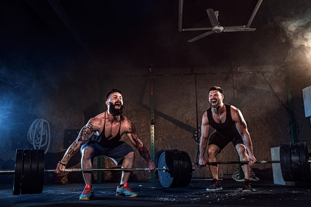 Two muscular bearded tattoed athletes training at gym