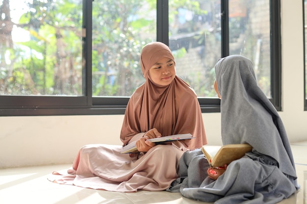 두 명의 아시아 무슬림 소녀가 모스크 안에서 코란을 읽은 후 대화를 나누고 있습니다.