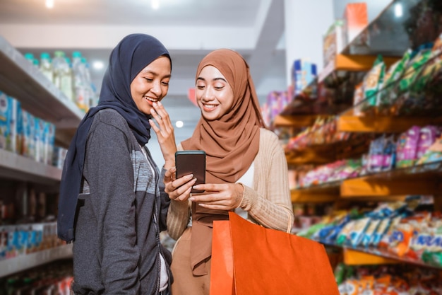 Two muslim girls using a smartphone while shopping together in a supermarket