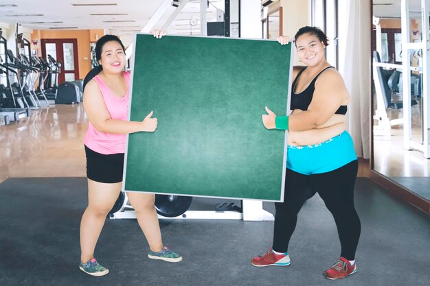 Two obese women lifting an empty board in gym