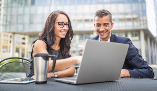 Two office, administration, finance or lawyers discuss work strategy looking into a laptop outdoors, smiling.