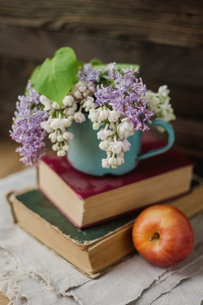 Two old books, apple and rusty mug with lilac bouquet on homespun napkin. 