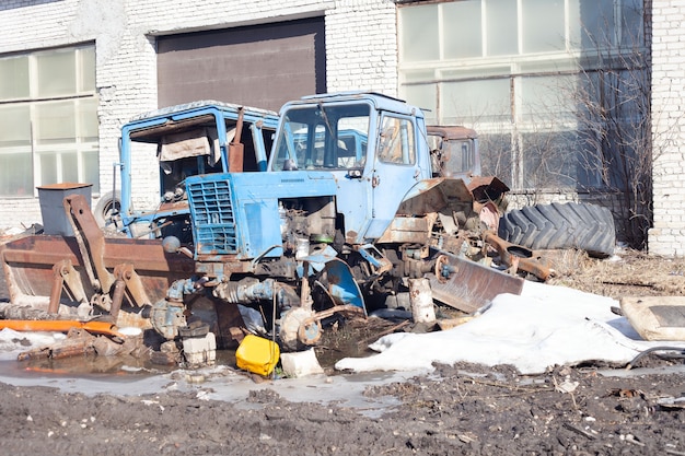 Фото Весной снаружи стоят два старых сломанных синих трактора.