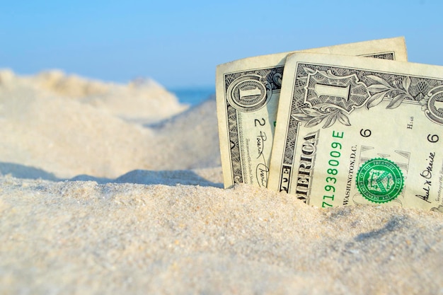 Photo two old dollar bills in sand on background of sea blue sky on sunny summer day dirty dollars closeup money grows from sand abstract concept money business pay finance vacation rest travels tourism