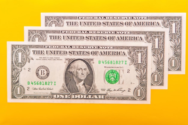 Two one dollar bills are sitting on a yellow background