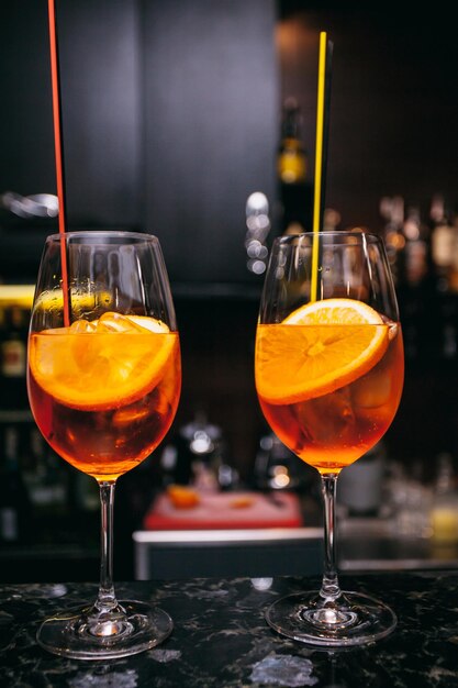 two orange alcoholic cocktails Aperol Spritz with cherries, orange zest on a dark background,