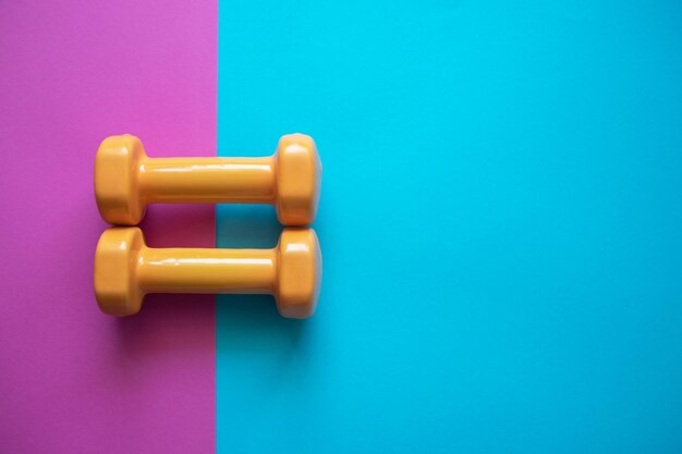 Two orange dumbbells on a pink and blue background with copy space A tool for training sport and activity in summer time