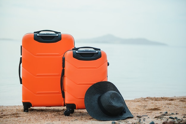 Two orange suitcases with a black hat on the sand of the beach