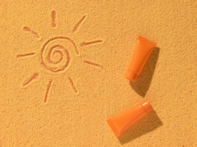 자외선 차단제의 두 개의 주황색 튜브와 모래에 그려진 태양. 자외선 차단 크림.